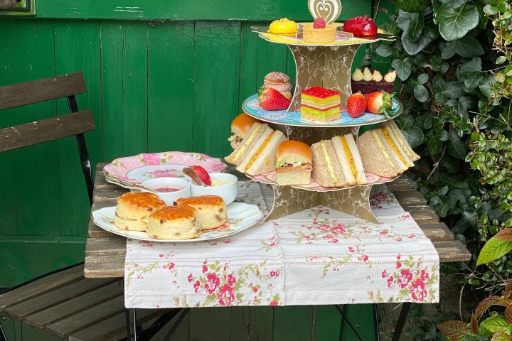 Afternoon tea setup on a rustic table with sandwiches, scones, and desserts.