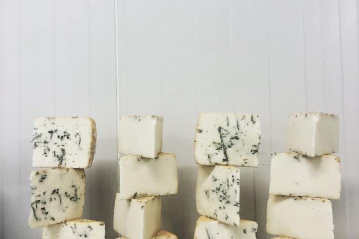 Four stacks of speckled cheese blocks against a white panel background.