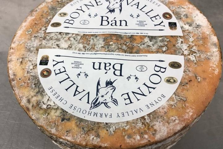 Round cheese with labels 'Boyne Valley Bán Farmhouse Cheese' on a gray surface.