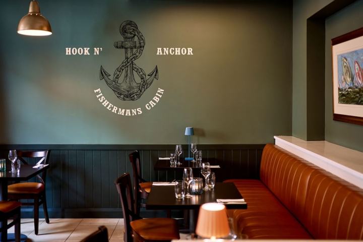 Cozy restaurant interior with green walls and nautical decor, featuring an anchor design and brown seating.