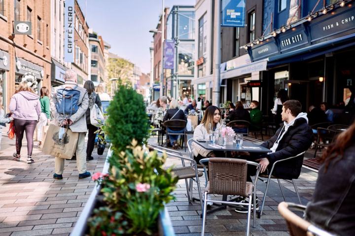 People dining and walking on busy pedestrian street with shops and cafes.