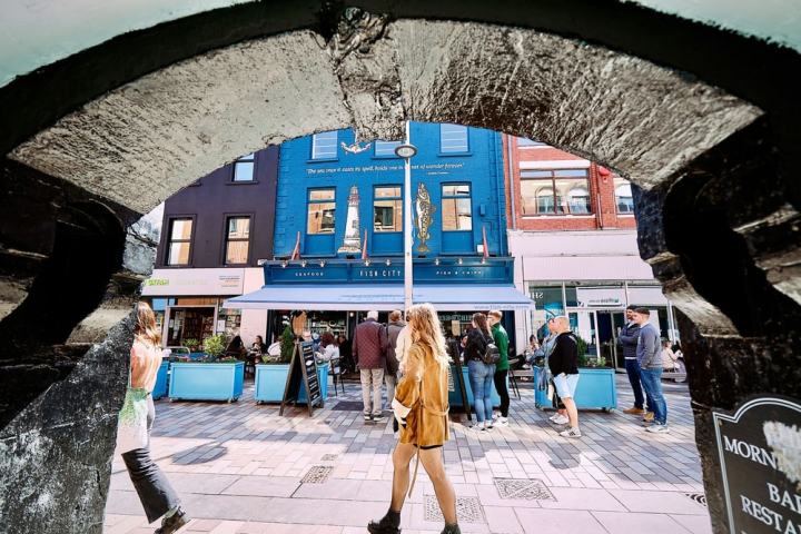 People walking past a blue fish and chips restaurant viewed through an archway.