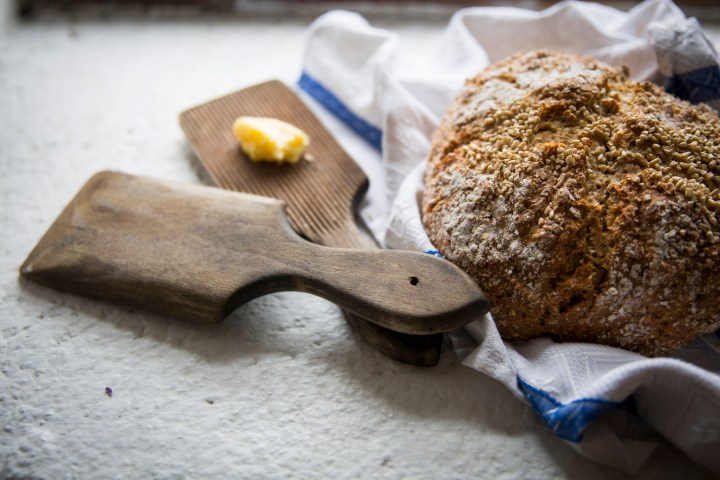 Fresh bread on towel with butter on a small wooden board nearby.