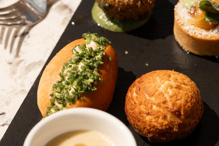 Assorted appetizers on a slate board with cup of soup, bread, and savory pastries.