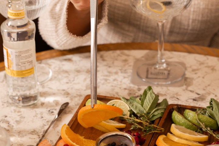 Person using tongs to pick up orange slice from tray with fruit slices and herbs.