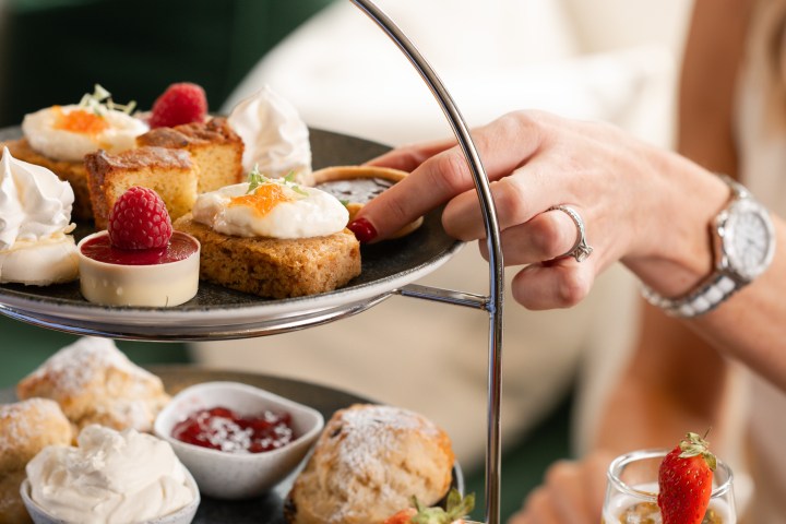 Person selecting dessert from three-tier afternoon tea stand with champagne.