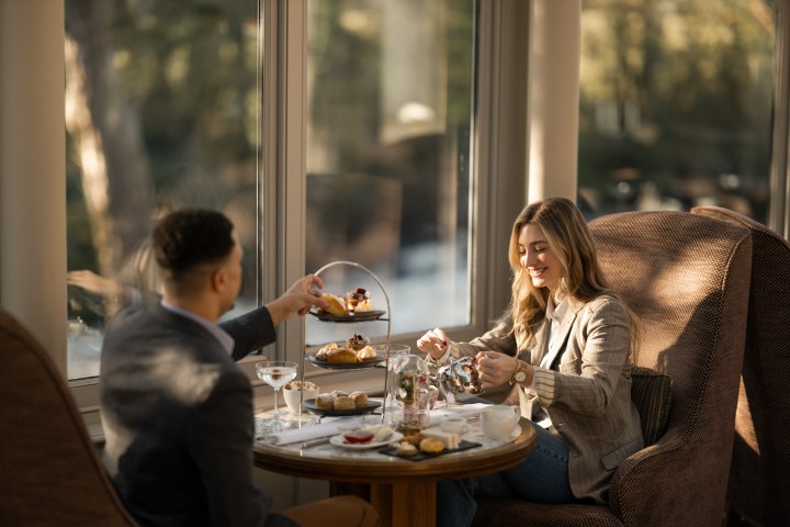 A couple enjoys afternoon tea with pastries by a window in a cozy setting.