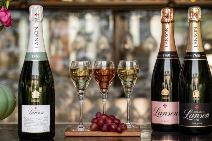 Four bottles of Lanson champagne with glasses and grapes on a wooden board.