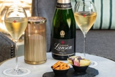 Table with champagne bottle, two glasses, candle, and snacks.