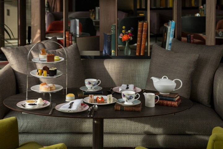 Afternoon tea setup with pastries and teapot on a table next to a sofa.