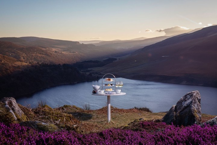 Afternoon tea setup on a small table overlooking a lake with scenic hills at sunset.