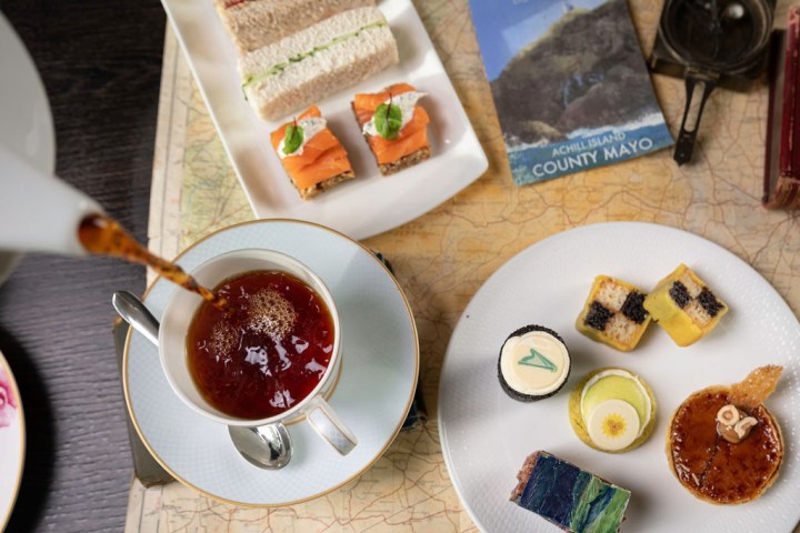 An overhead view of tea being poured, sandwiches, and desserts on a map.