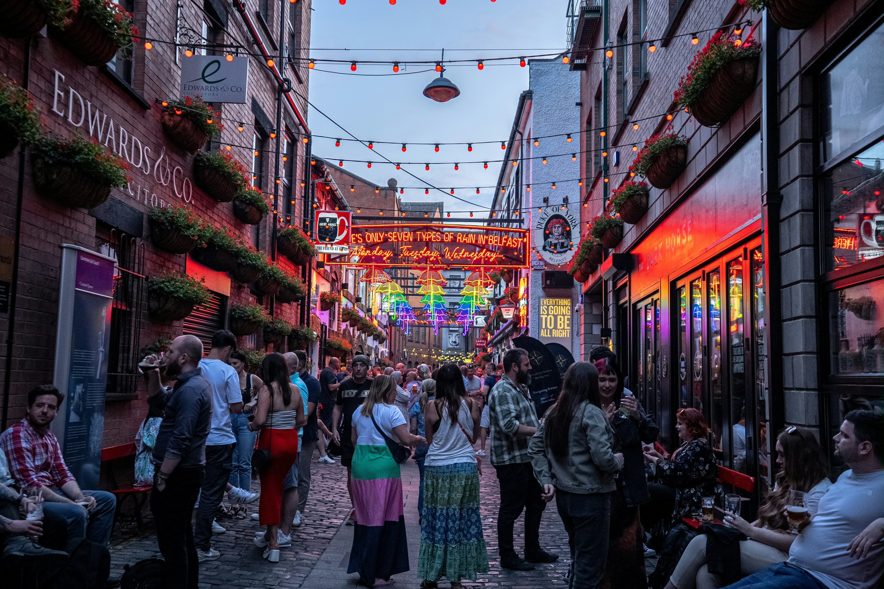 Crowded alleyway with neon lights and people socializing outdoors.