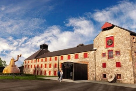 Historic distillery building with red windows, copper still, and blue sky.