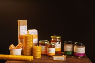 Assorted honey jars, beeswax candles, and honeycomb on a wooden surface.