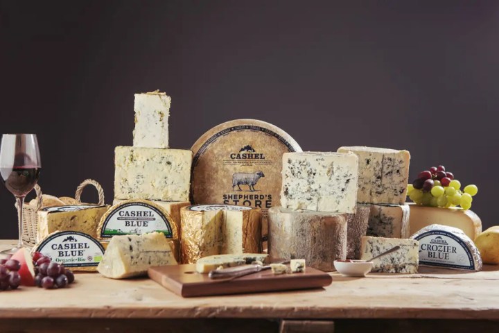 Variety of cheeses and a glass of red wine on a wooden table.