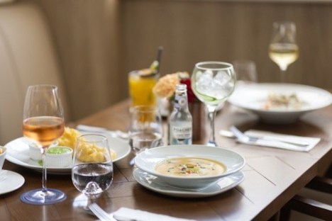 Table with plates of soup, wine glasses, and snacks set for a meal.
