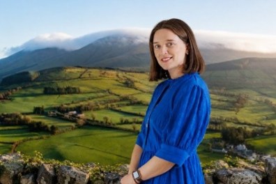 Woman in blue dress stands before mountainous landscape.