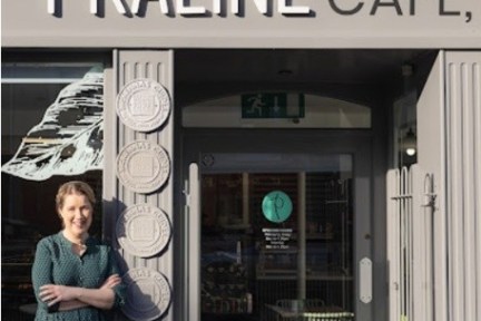 Person standing outside Praline Café storefront, smiling with arms crossed.