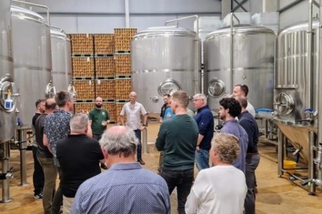 Group of people touring a brewery with large stainless steel tanks.