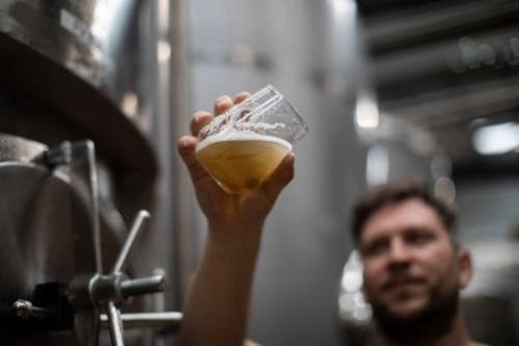 Man holding a tilted glass of beer in a brewery for inspection.