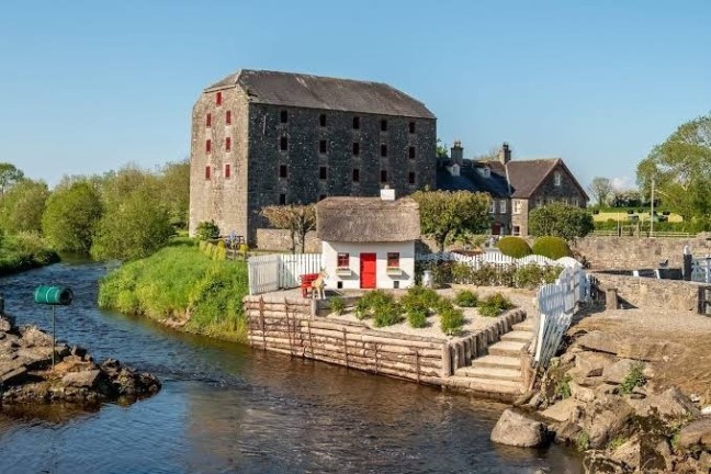 Historic mill and small cottage by a river with blue sky.