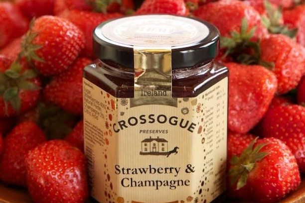 Jar of strawberry and champagne preserve on a plate of fresh strawberries.